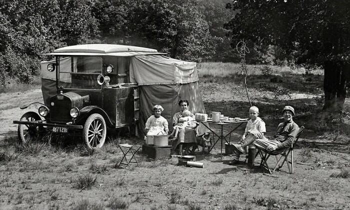 People sitting around a table next to their car. The people are positioned looked at the camera