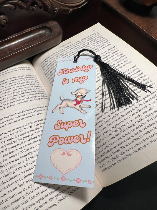 A bookmark sitting on an open book with the words anxiety is my super power and a lamb centered on the book mark and a heart at the bottom